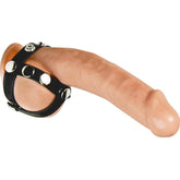 A black PU leather and metal cock and ball harness with adjustable straps and metal studs, worn around the penis and scrotum.