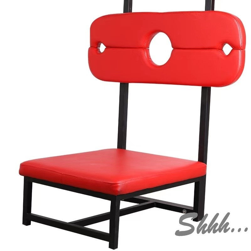 A black and red upholstered BDSM stocks stool with a red cushion and a black steel frame, designed for restraint play.