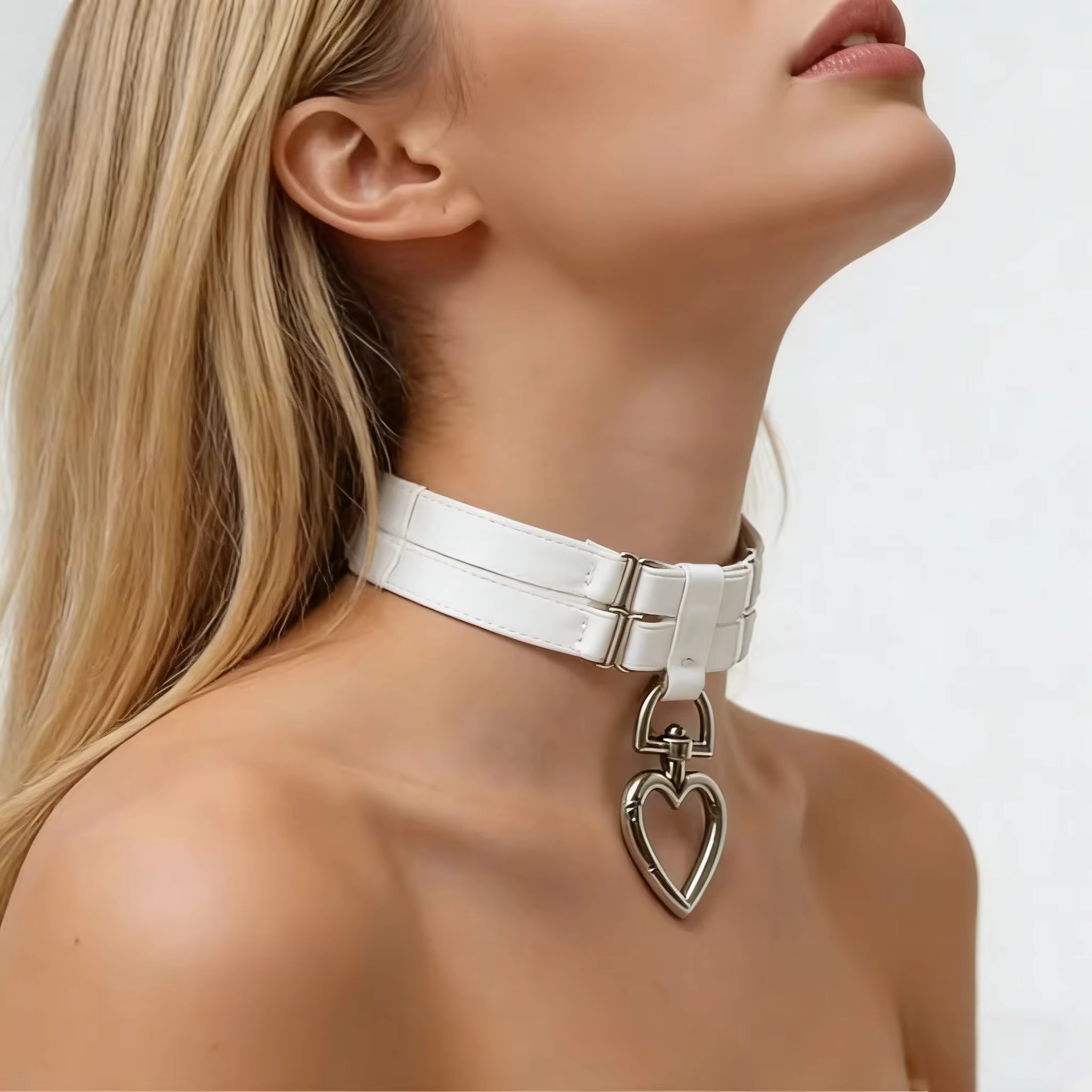Close-up of a woman wearing a white choker with a heart-shaped pendant on a plain background